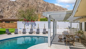 Ein Swimmingpool mit Liegestühlen und einer Pergola, umgeben von einem angelegten Garten und einem Bergpanorama.