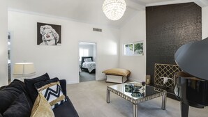 Ein modernes Wohnzimmer mit einem schwarzen Sofa, einem Glastisch, einem Klavier und einer großen Kronleuchter.