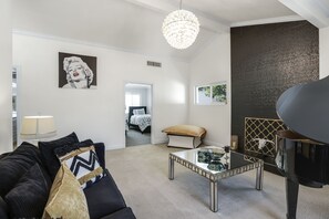 Un salon moderne avec un canapé noir, une table basse en verre, un piano et un grand lustre.