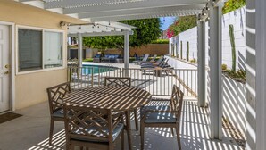 Eine überdachte Terrasse mit Pool, Gartenmöbeln und einem weißen Zaun.