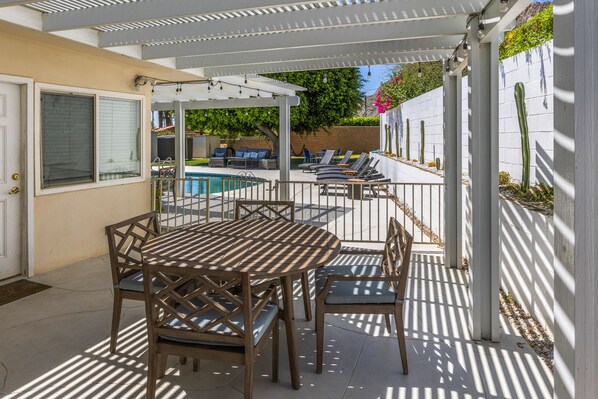 Une terrasse couverte avec une piscine, du mobilier d’extérieur et une clôture blanche.