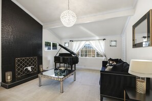 Un salon avec un grand piano, une table basse en verre, un canapé noir et un lustre.