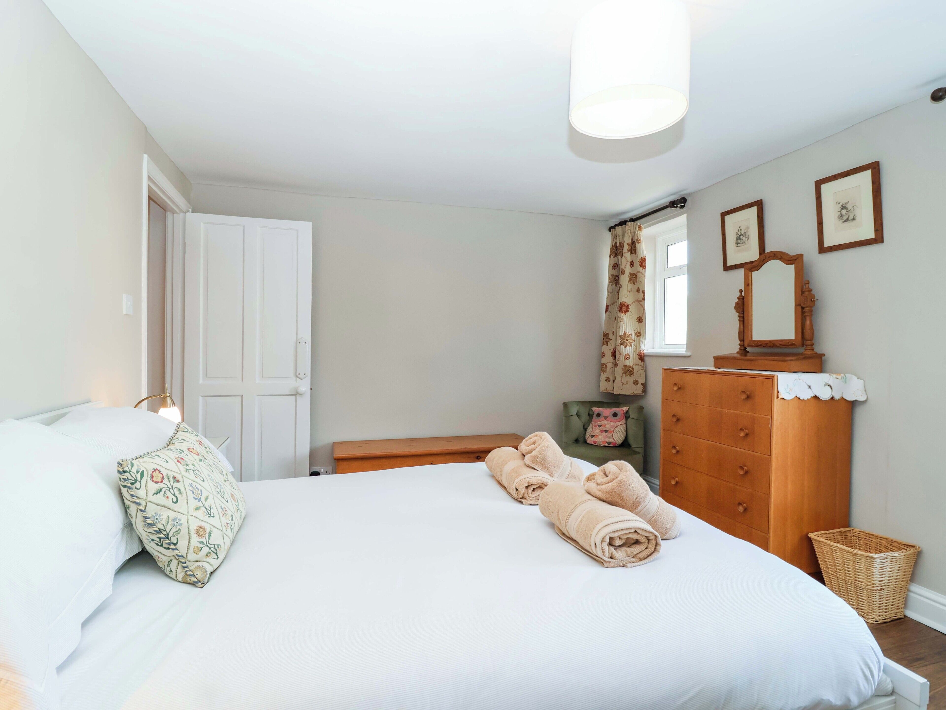 Un dormitorio con cama, cómoda, espejo y ventana con cortinas.