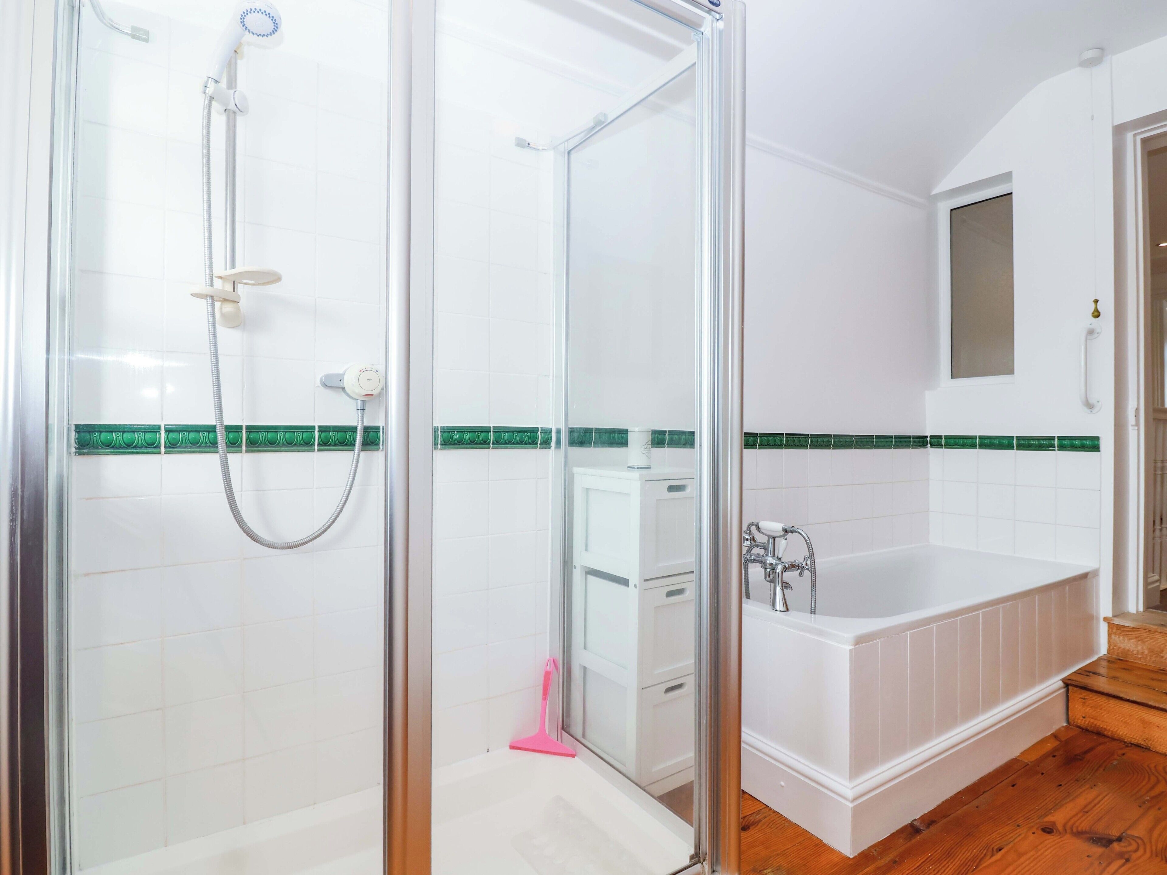 A bathroom with a glass-enclosed shower, a white bathtub, and a green-tiled backsplash.
