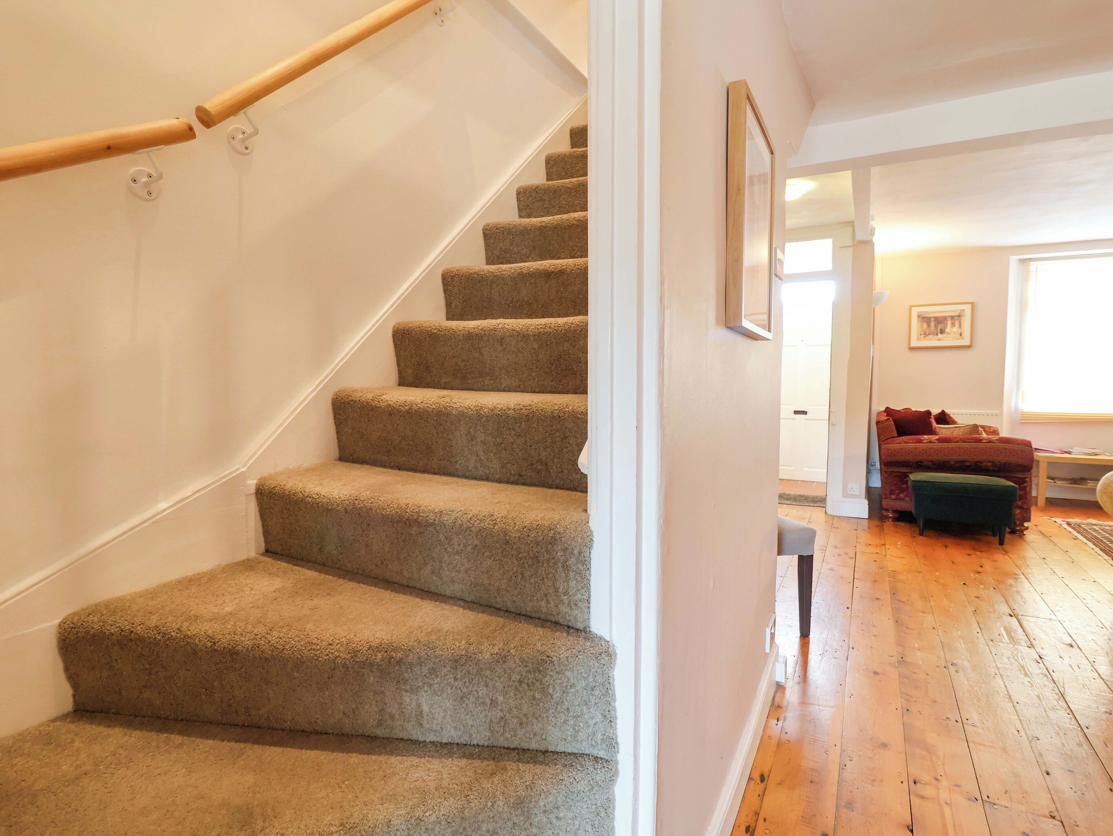 A carpeted staircase with a wooden handrail, leading to a room with a wooden floor and a red sofa.