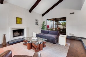A modern living room with a fireplace, a glass coffee table, a sofa, and a view of the outdoors.