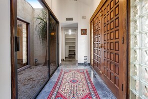 A hallway with a patterned rug, a wooden door, and a glass door leading to an outdoor area.