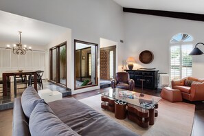 A modern living room with a sofa, coffee table, and a dining area with chairs and a table.