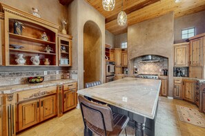 A spacious kitchen with wooden cabinets, a large island, and a stone backsplash. - Luxury home with a pool, spa, fireplace, & private gas grill (Goodyear)
