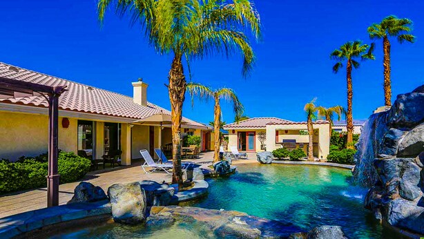 A resort with a pool, palm trees, and a building with a tiled roof. - Luxurious home with an outdoor kitchen, private pool & spa - close to golf (Bermuda Dunes)