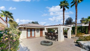 A patio area with a stone fire pit, outdoor seating, and palm trees. - Luxurious home with an outdoor kitchen, private pool & spa - close to golf (Bermuda Dunes)