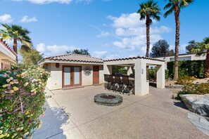 A patio area with a stone fire pit, outdoor seating, and palm trees. - Luxurious home with an outdoor kitchen, private pool & spa - close to golf (Bermuda Dunes)