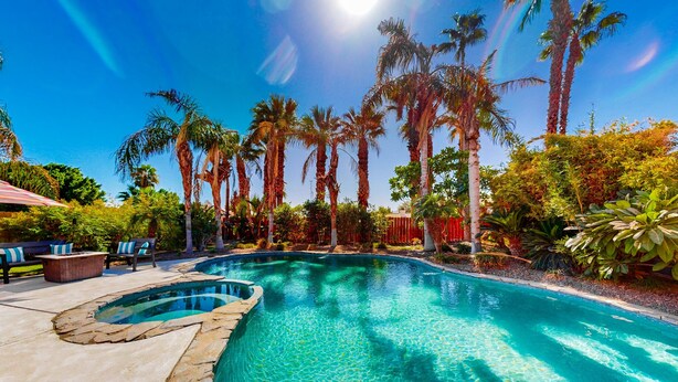 A swimming pool with clear blue water, surrounded by palm trees and a patio area with outdoor furniture. - Dog-Friendly Home w/ a Private Pool, Pool Spa, Firepit, & Patio - 3BR - #66716 (La Quinta)