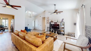 A spacious living area with a leather sofa, a television, ceiling fans, and a fireplace. - Dog-Friendly Home w/ a Private Pool, Pool Spa, Firepit, & Patio - 3BR - #66716 (La Quinta)