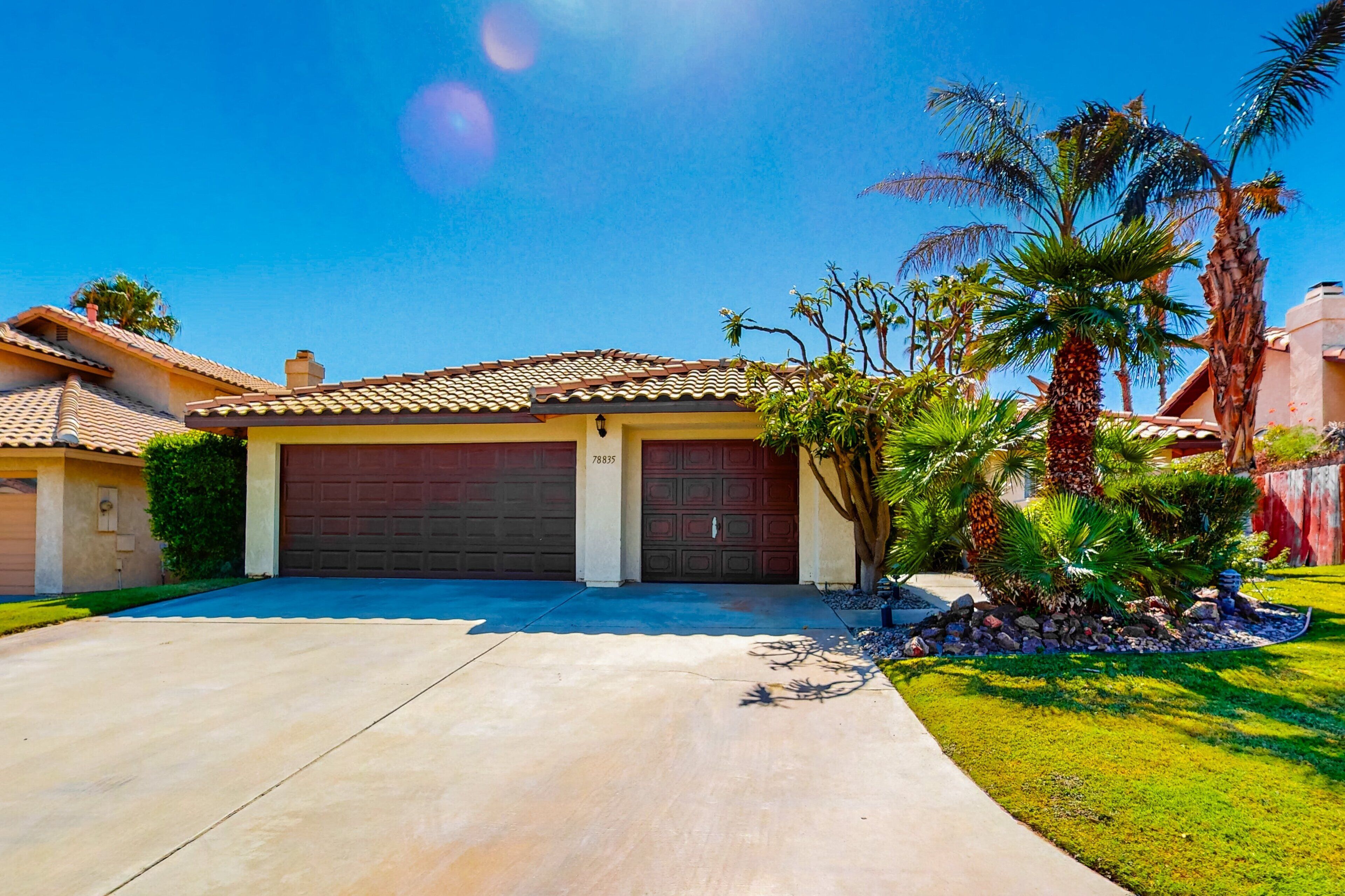 A residential house with a tiled roof, two garage doors, and a well-maintained lawn with palm trees.