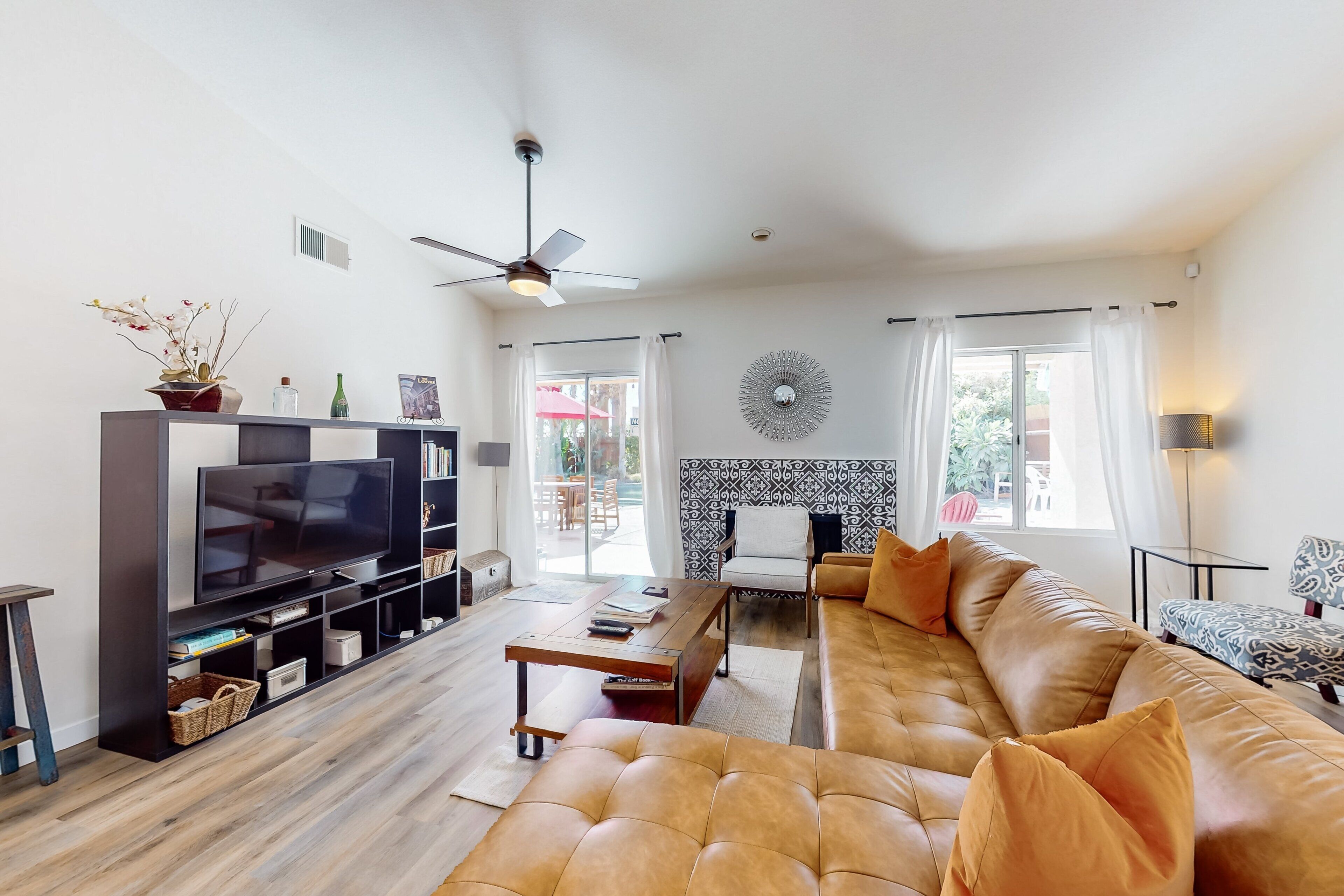 A living room with a large leather sofa, a flat-screen TV, a ceiling fan, and a decorative wall piece.