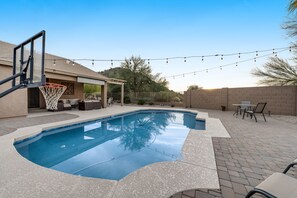 Un jardin avec une piscine, un panier de basketball et du mobilier d’extérieur.