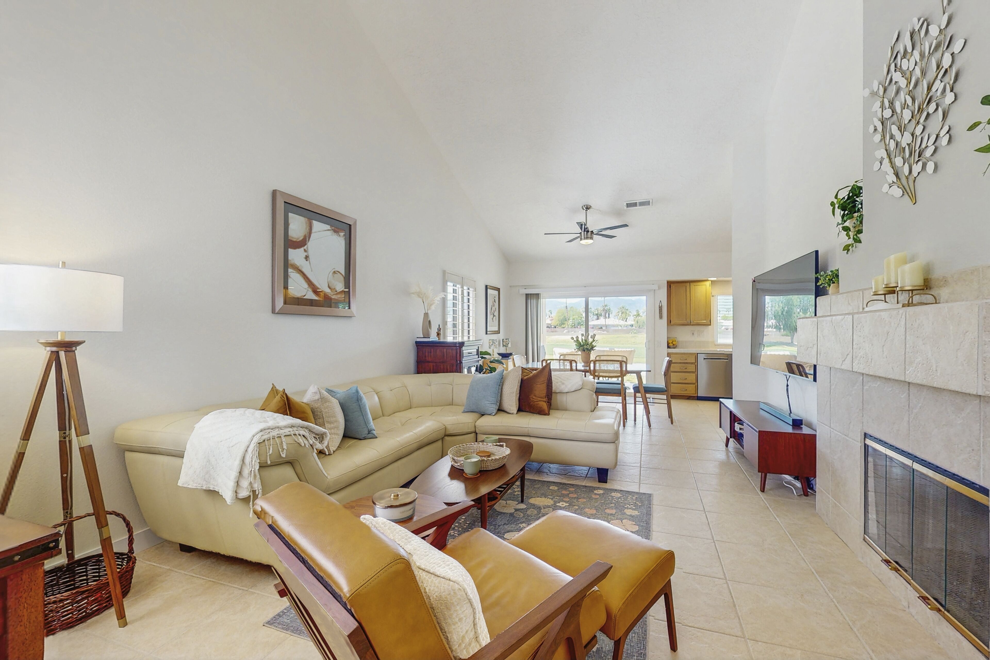 A spacious living room with a sectional sofa, a coffee table, and a fireplace. There is a dining area with a table and chairs, and a kitchen in the background.