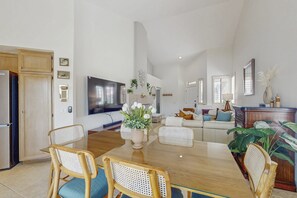 A spacious living area with a dining table, chairs, a flat-screen TV, and a sofa. - Sun, Comfort, and Stunning Views, Shared pool & Dog-friendly (Palm Desert)