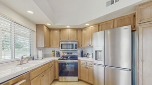 A modern kitchen with wooden cabinets, stainless steel appliances, and a large window providing natural light. - Sun, Comfort, and Stunning Views, Shared pool & Dog-friendly (Palm Desert)