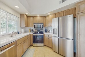A modern kitchen with wooden cabinets, stainless steel appliances, and a large window providing natural light. - Sun, Comfort, and Stunning Views, Shared pool & Dog-friendly (Palm Desert)