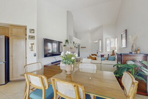 Ett rymligt vardagsrum med ett matbord, flätade stolar, en platt-TV och en soffa.