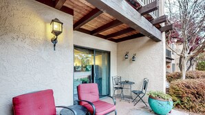 A patio with two red chairs, a table, and a large planter. - Stylish ground floor condo - patio, pool, fireplace, full kitchen & washer/dryer (Sedona)