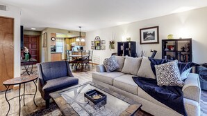 A living room with a sofa, armchair, coffee table, and a dining area with chairs and a table. - Stylish ground floor condo - patio, pool, fireplace, full kitchen & washer/dryer (Sedona)