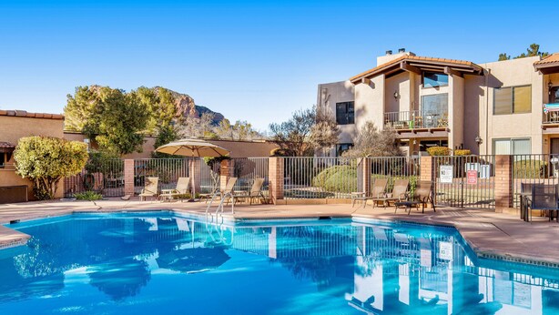 A swimming pool with a clear blue water, surrounded by a fence, and adjacent to a building with a balcony. - Stylish ground floor condo - patio, pool, fireplace, full kitchen & washer/dryer (Sedona)