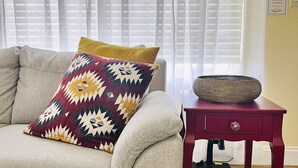 Un divano beige con un cuscino decorato e un tavolino rosso con un cesto intrecciato.