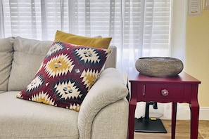 A beige sofa with a patterned pillow and a red side table with a woven basket. - South Mountain home with pool, grill, fireplace & fast WiFi - snowbird-friendly (Phoenix)