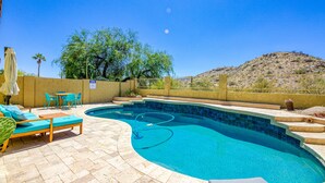 Una piscina con bordo curvo, circondata da una terrazza con lettini e un tavolo.