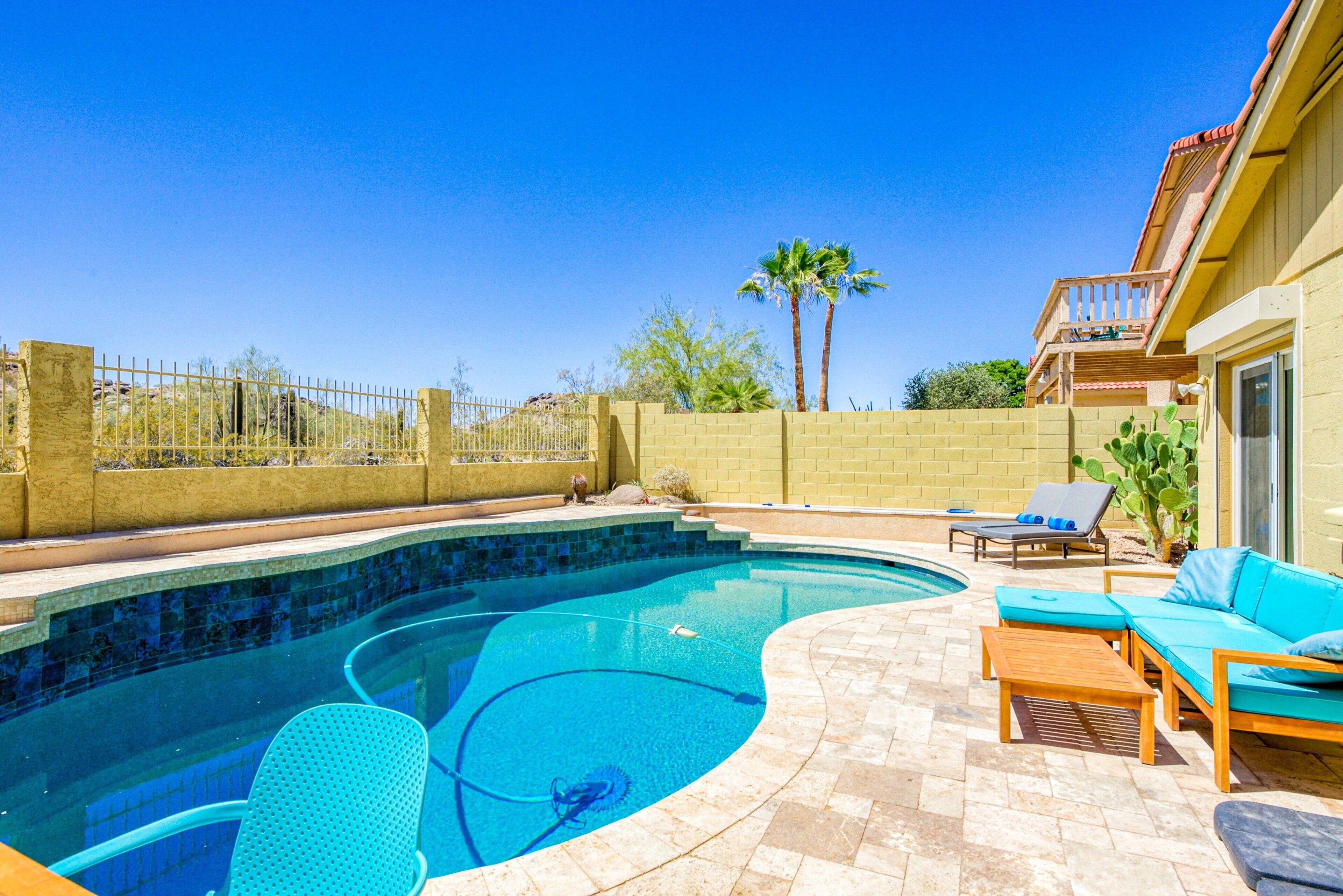 A swimming pool with a tiled edge, surrounded by a patio area with a wooden deck, a built-in bench, and a small table.