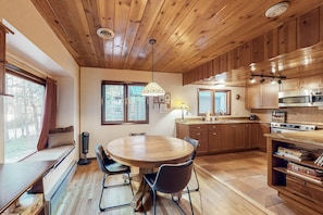 A cozy kitchen with wooden cabinets, a dining table with chairs, a built-in stove, and a window with curtains.