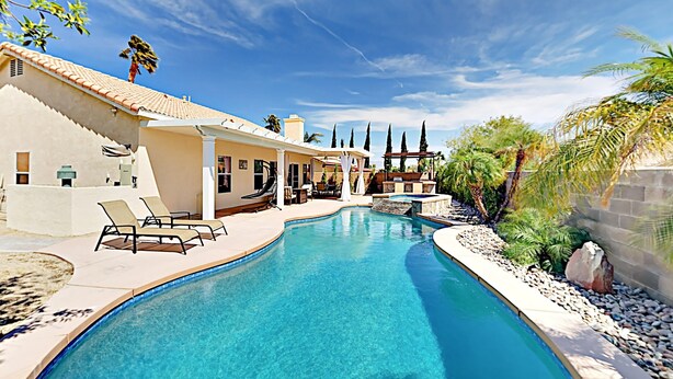 A swimming pool with lounge chairs, a covered seating area, and a building with a tiled roof. - Stunning home  with private heated pool, spa, firepit, grill & alfresco dining (Cathedral City)
