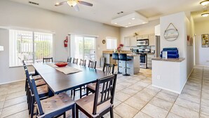 A spacious dining area with a long table and chairs, a kitchen with modern appliances, and a ceiling fan. - Stunning home  with private heated pool, spa, firepit, grill & alfresco dining (Cathedral City)