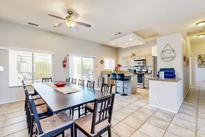 A spacious dining area with a long table and chairs, a kitchen with modern appliances, and a ceiling fan. - Stunning home  with private heated pool, spa, firepit, grill & alfresco dining (Cathedral City)