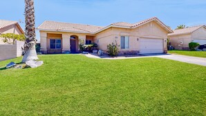 A residential house with a well-maintained lawn, a palm tree, and a garage. - Stunning home  with private heated pool, spa, firepit, grill & alfresco dining (Cathedral City)