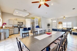 A spacious kitchen with modern appliances, a dining area with a long table, and a living room with a sofa and TV. - Stunning home  with private heated pool, spa, firepit, grill & alfresco dining (Cathedral City)