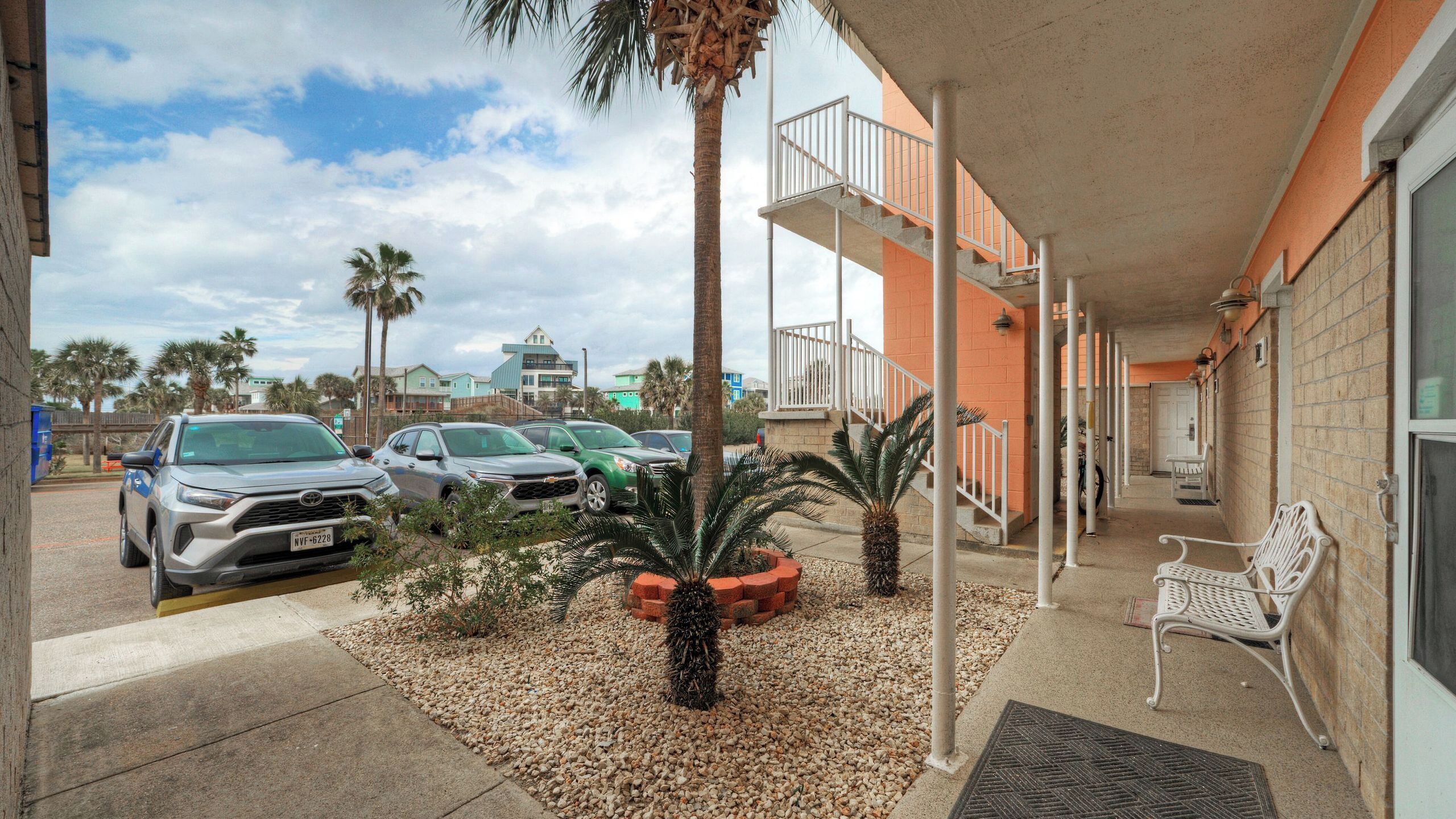 A building with a covered parking area, a staircase, and a bench.
