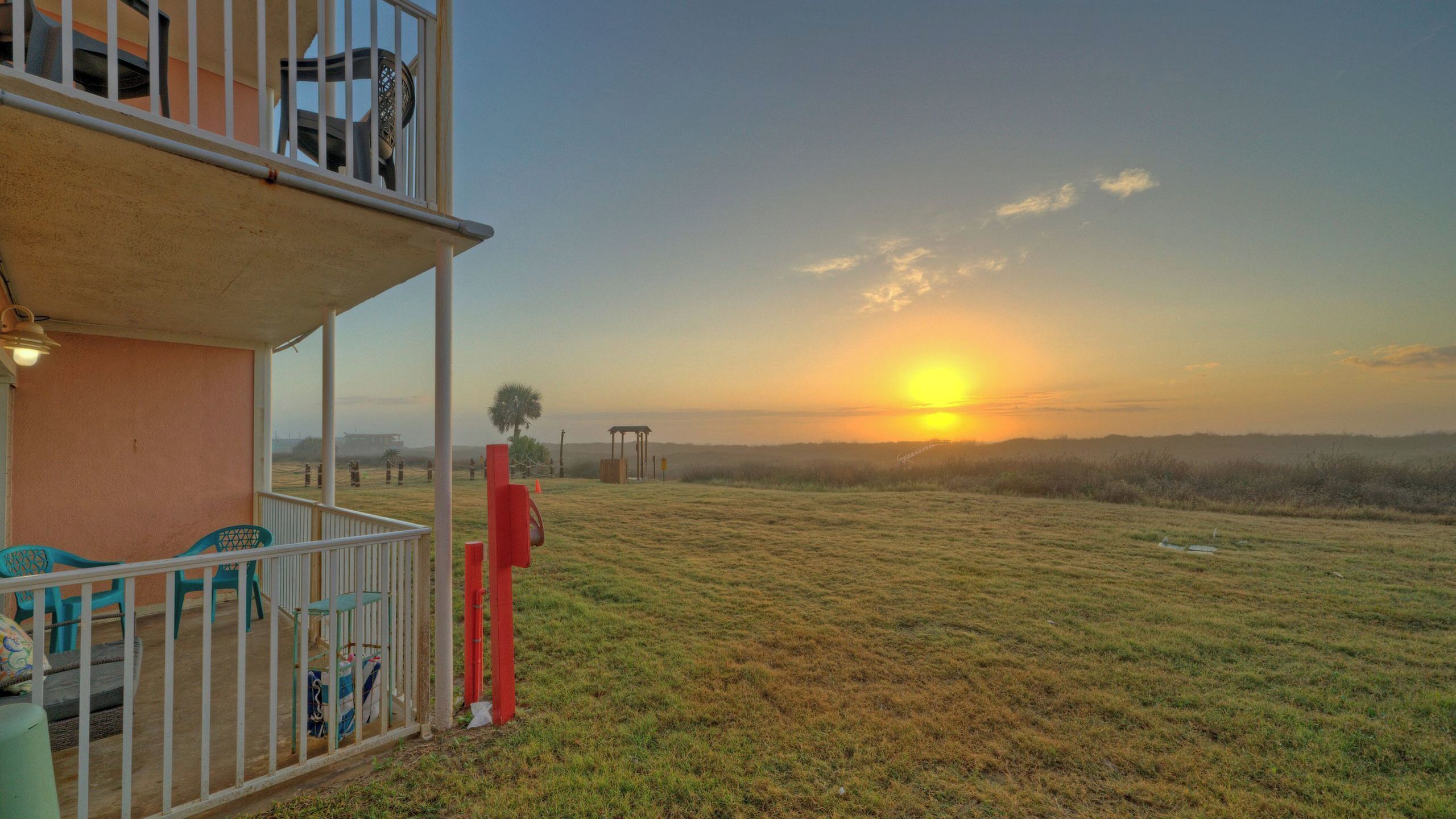 Un balcon offrant une vue sur le coucher de soleil au-dessus d’un champ verdoyant.