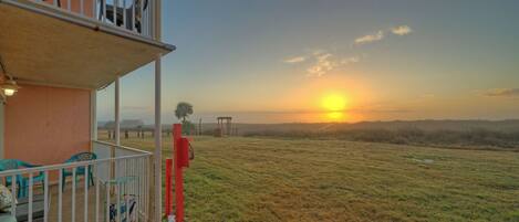 A balcony with a view of the sunset over a grassy field.