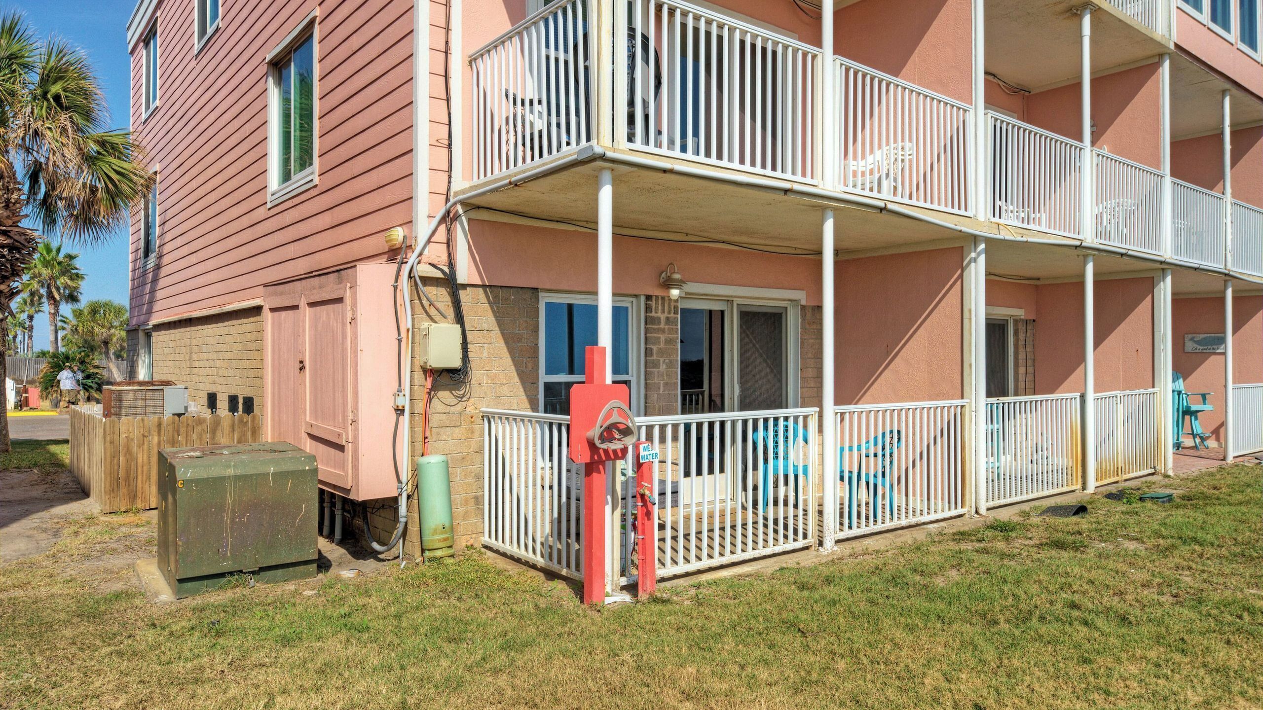 A multi-story building with a balcony, a water pump, and a wooden fence.