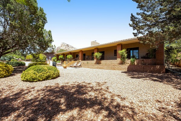 A two-story building with a covered patio area, surrounded by landscaped gardens and trees. - Red Rock-view oasis with beautiful veranda, central AC, W/D (Sedona)