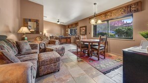 A spacious living area with a large sofa, ottoman, and dining table set. There is a window with a view of a natural landscape. - Red Rock-view oasis with beautiful veranda, central AC, W/D (Sedona)