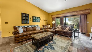 A living room with a brown leather sectional sofa, a wooden coffee table, and a patterned rug. There are two wall-mounted picture frames and a floor lamp. - Red Rock-view oasis with beautiful veranda, central AC, W/D (Sedona)