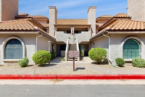 A two-story building with a tiled roof, a central staircase, and a sign with apartment numbers. - Inviting desert oasis with modern decor, pool, and hot tub (Scottsdale)