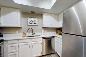 A kitchen with white cabinets, a stainless steel refrigerator, a dishwasher, and a skylight above the sink. - Inviting desert oasis with modern decor, pool, and hot tub (Scottsdale)