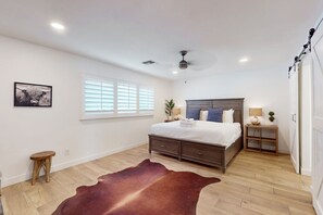 A bedroom with a large bed, a ceiling fan, a window with blinds, a small stool, and a cowhide rug. - Designer getaway with private pool, firepit, walled yard & RV parking (Scottsdale)