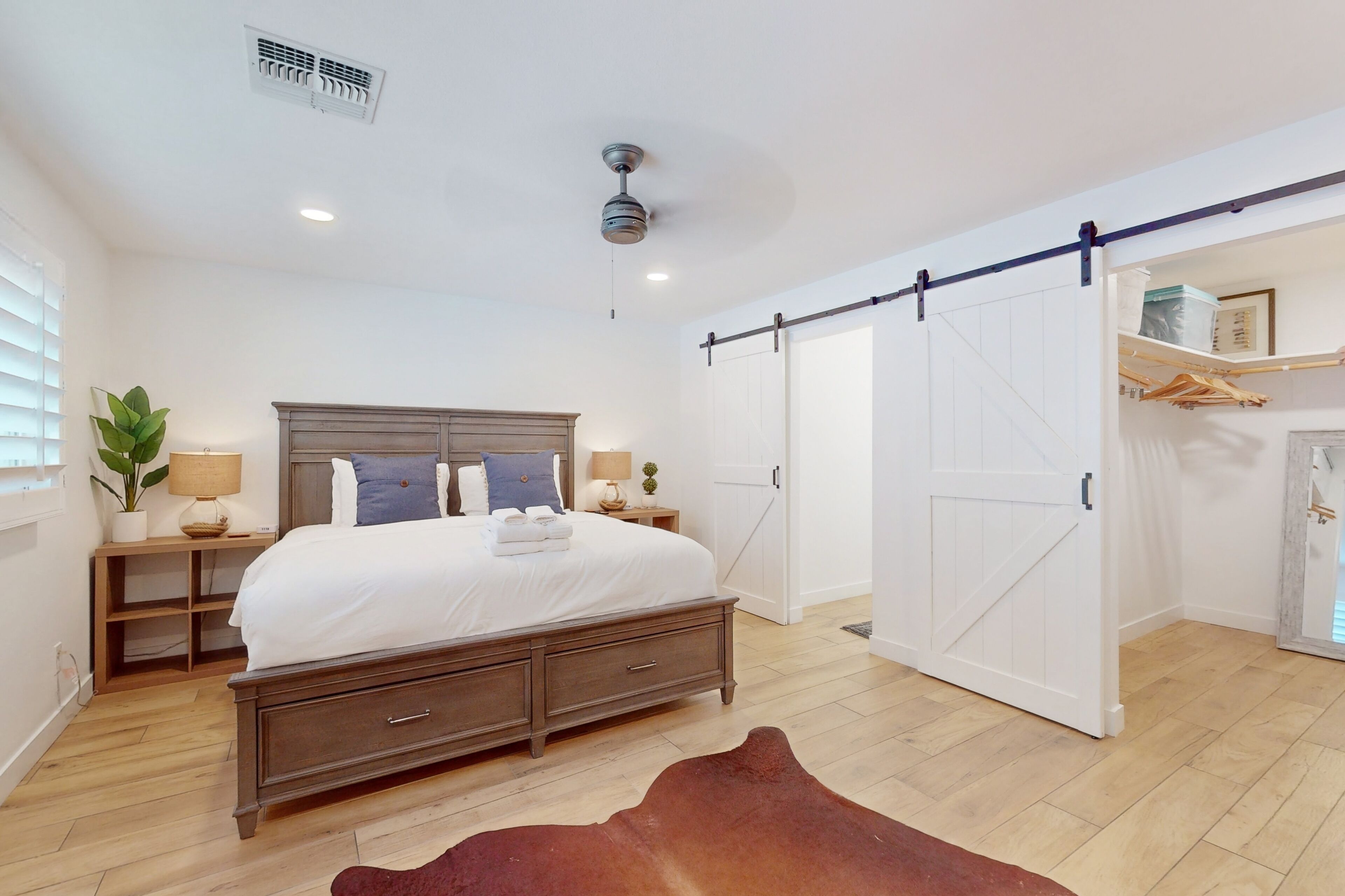 Une chambre à coucher comprenant un lit, des tables de chevet, une armoire, un ventilateur de plafond et une porte coulissante.